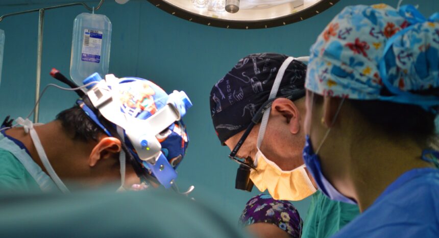 Mass shooting injuries: Four surgeons in the operating room bending over of an operating table, which is out of the frame.