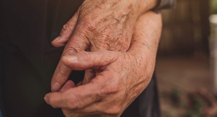 Two hands with wrinkled skin holding each other.