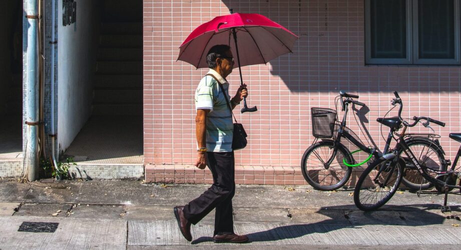 Man on street holding umbrella walking beneath an air conditioner