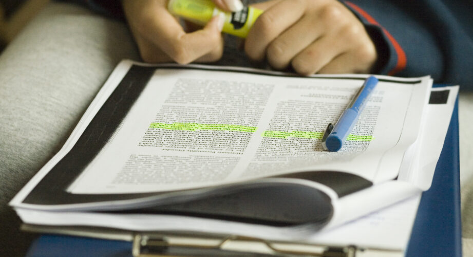 close-up of a woman's hand highlighting text on a paper.