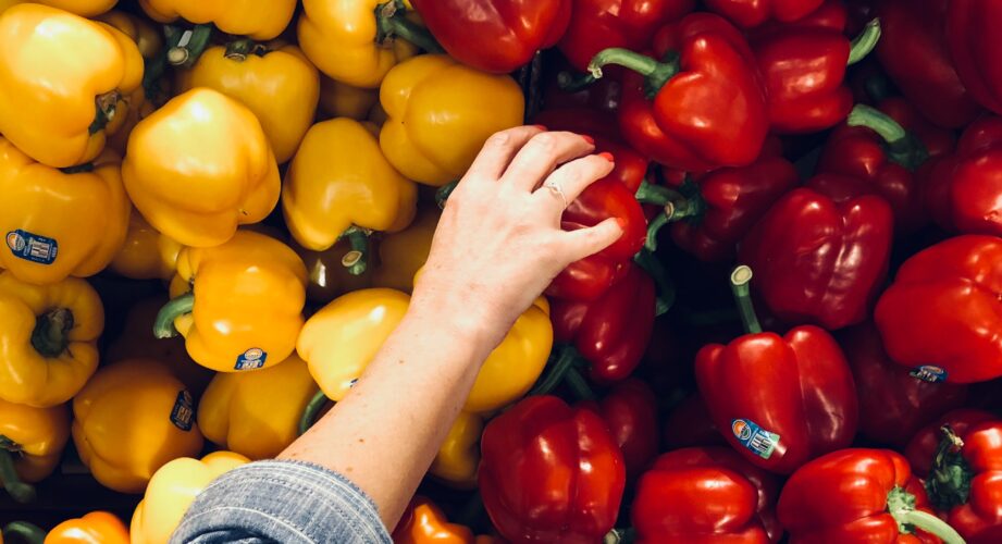 Arm reaching to pick a red bell pepper from a bunch of red and yellow bell peppers